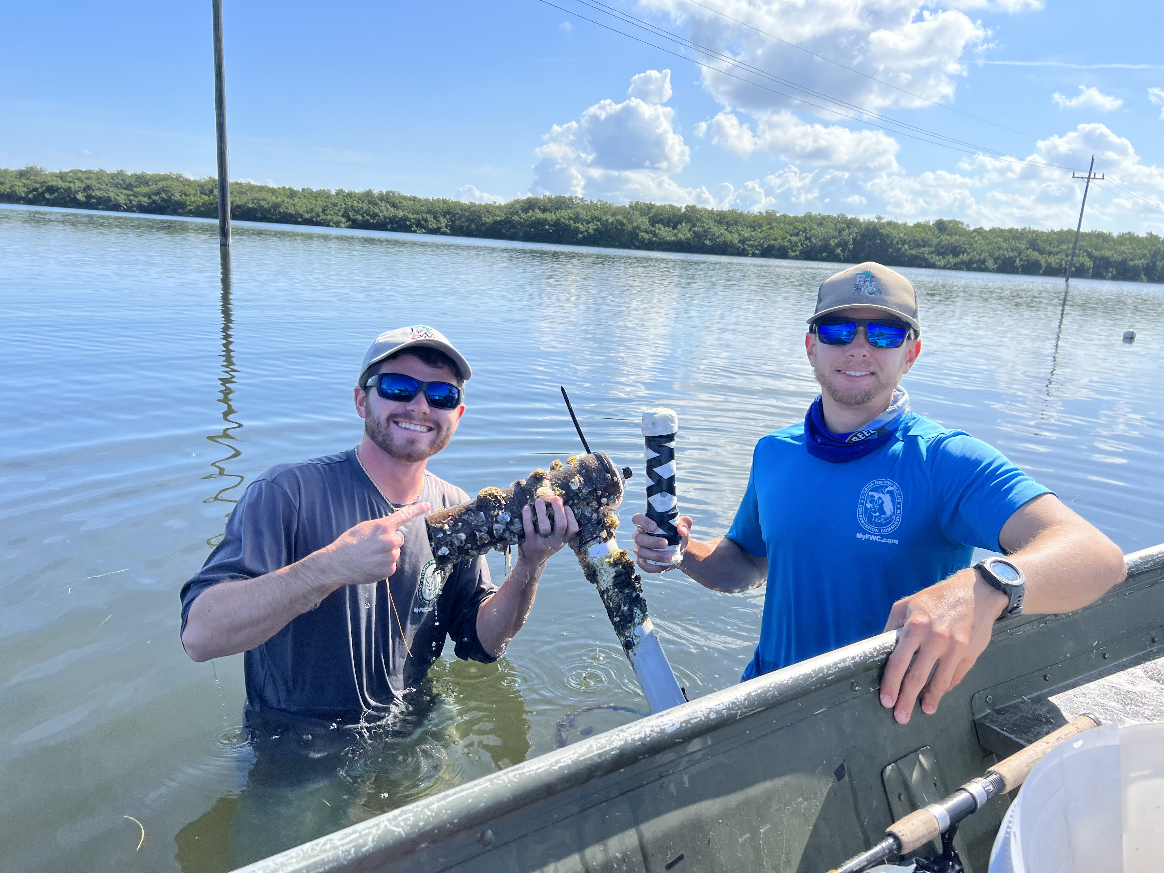 Two FWRI staff members standing in the water in Robinson Preserve, one holding the housing for an acoustic array and the other holding a water quality logger in its housing